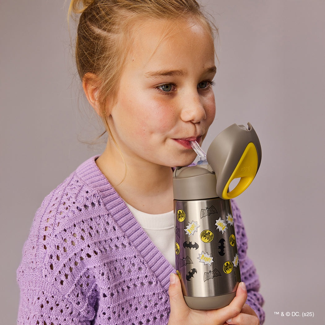 Young girl drinking from a Batman-themed tumbler against a plain background