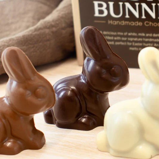 Chocolate bunnies in various colors on a wooden surface with a box labeled 'Bunny' in the background.