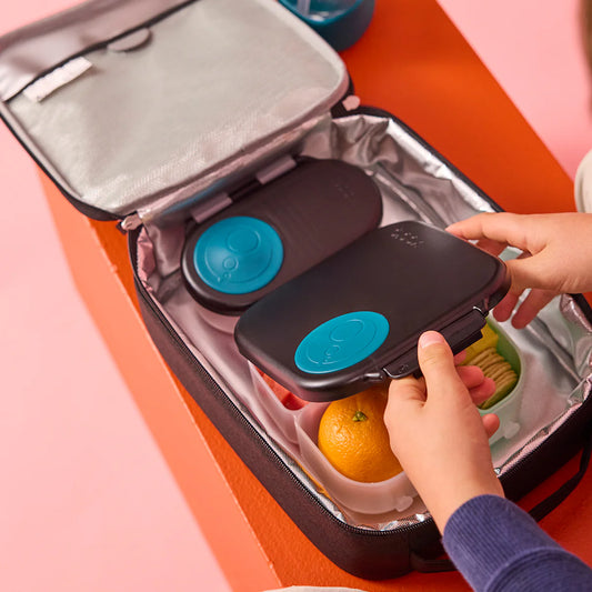 Person placing a black lid with blue circular designs into an open lunch bag.