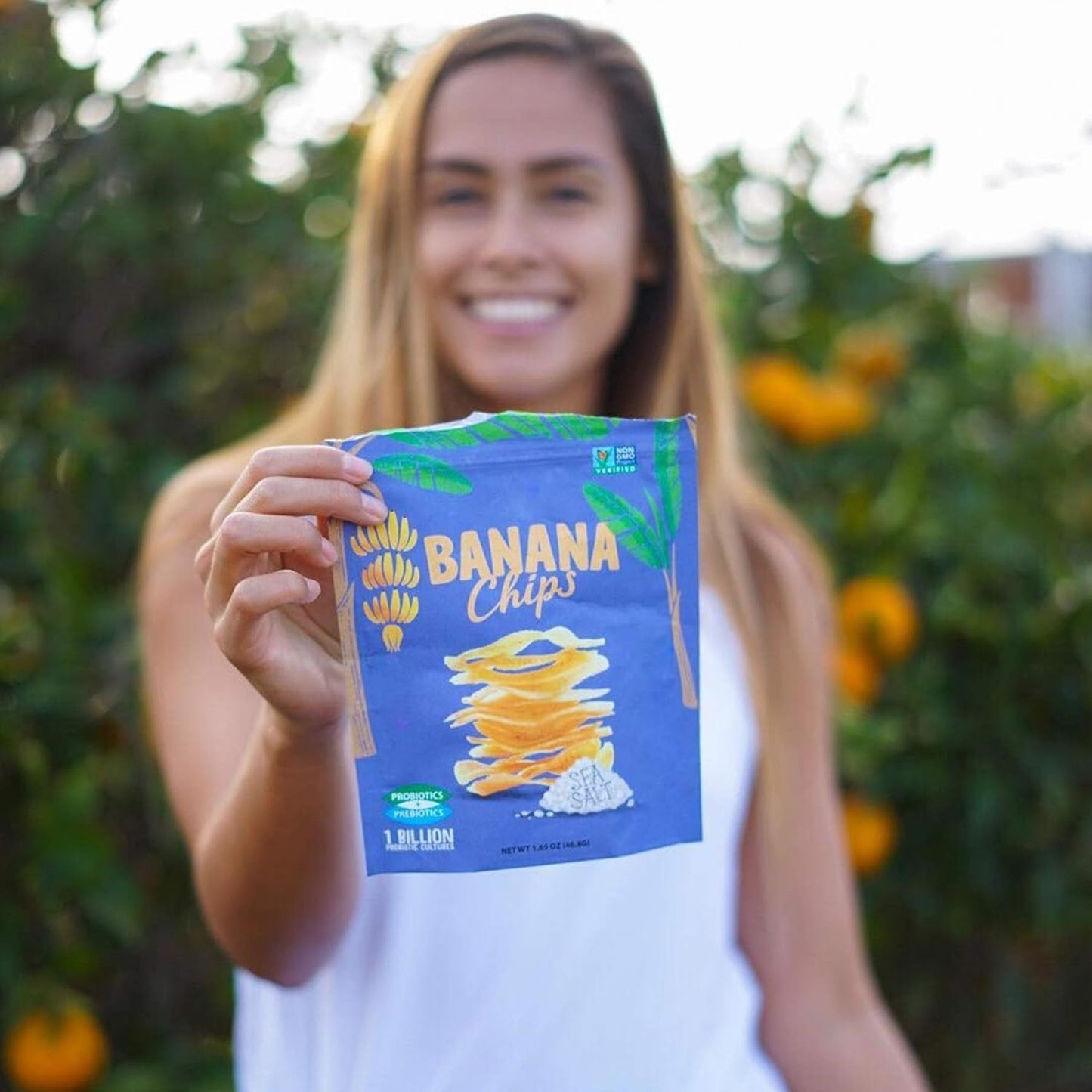 Person holding a package of banana chips with a blurred outdoor background