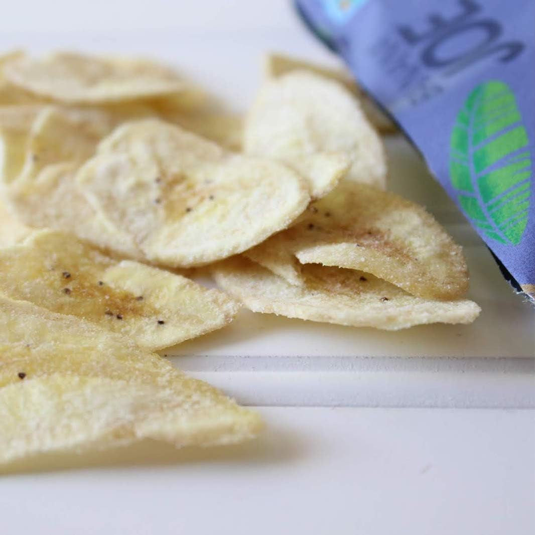 Pile of tortilla chips on a white surface with a blue snack bag in the background.