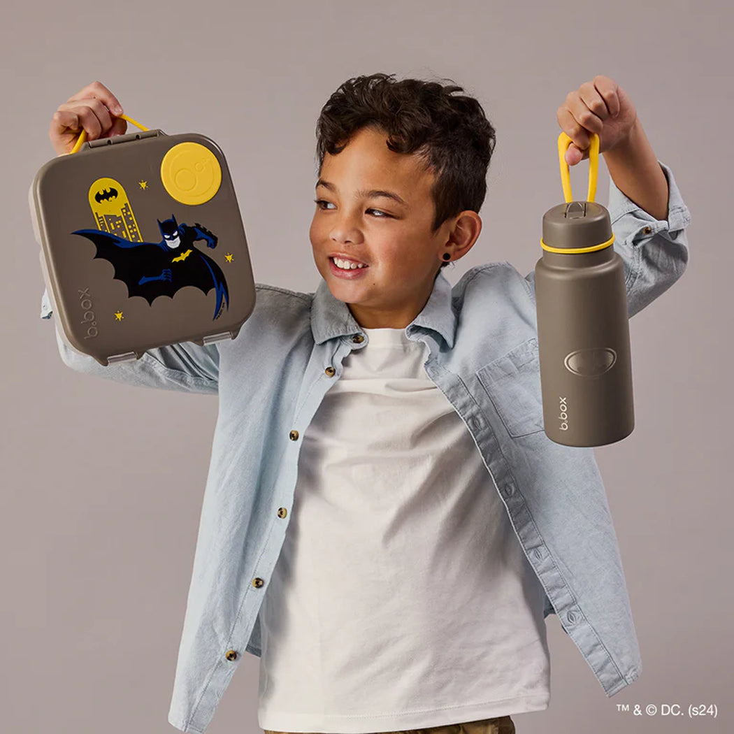 Child holding a Batman lunch box and water bottle against a plain background