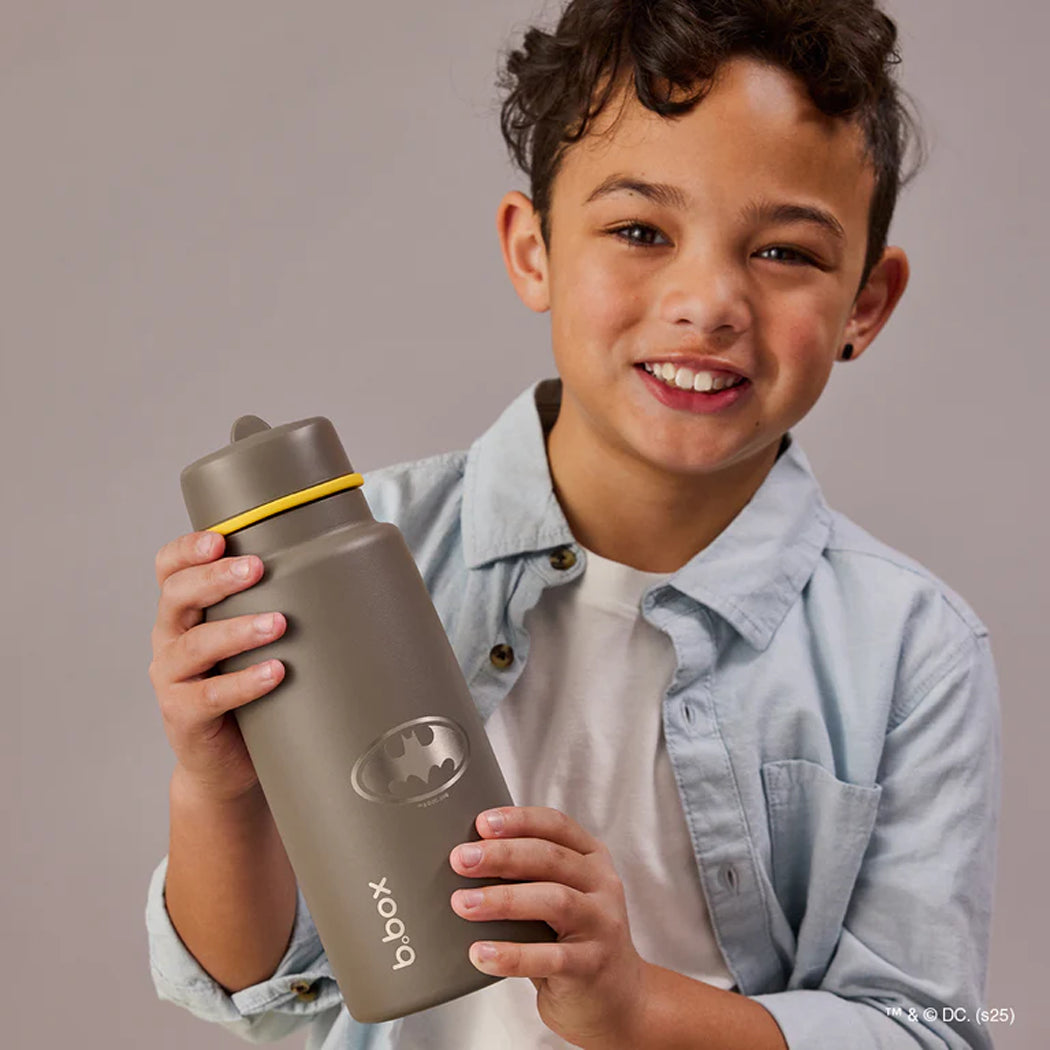 Child holding a gray water bottle with a yellow accent on a plain background