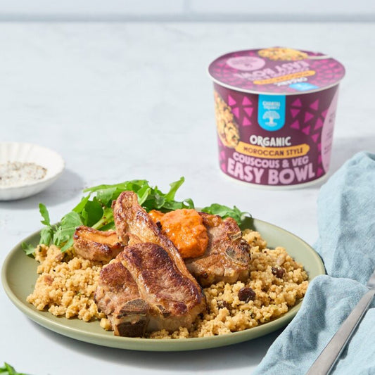 Plated dish with couscous, lamb chops, and vegetables next to a container of organic couscous and veg easy bowl.