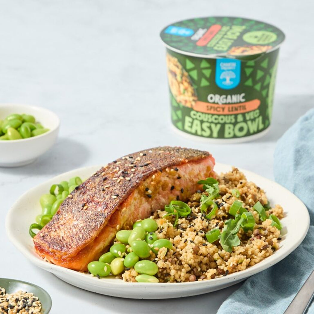 Plated dish with salmon, couscous, and edamame beans next to a container of organic food.