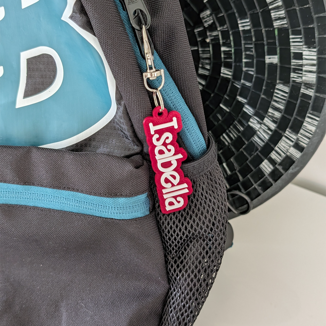 Backpack with a personalized name tag labeled 'Isabella' attached to it.