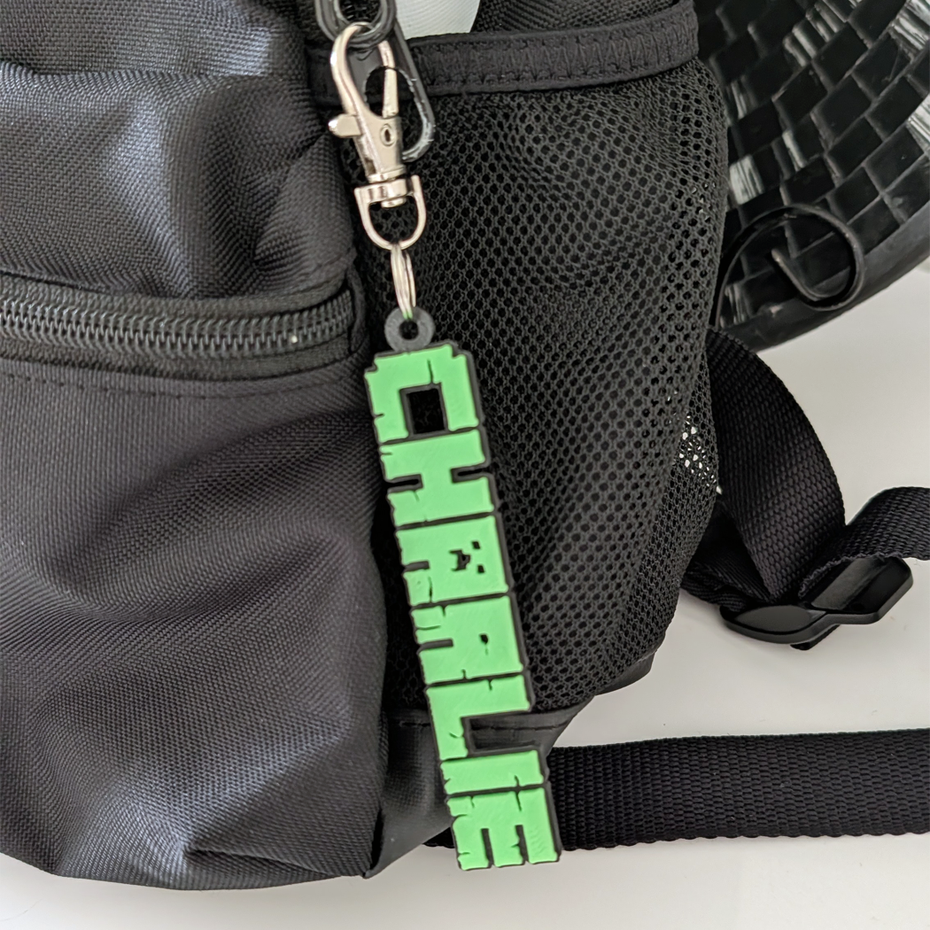 Black bag with a green keychain attached, featuring a pixelated design.