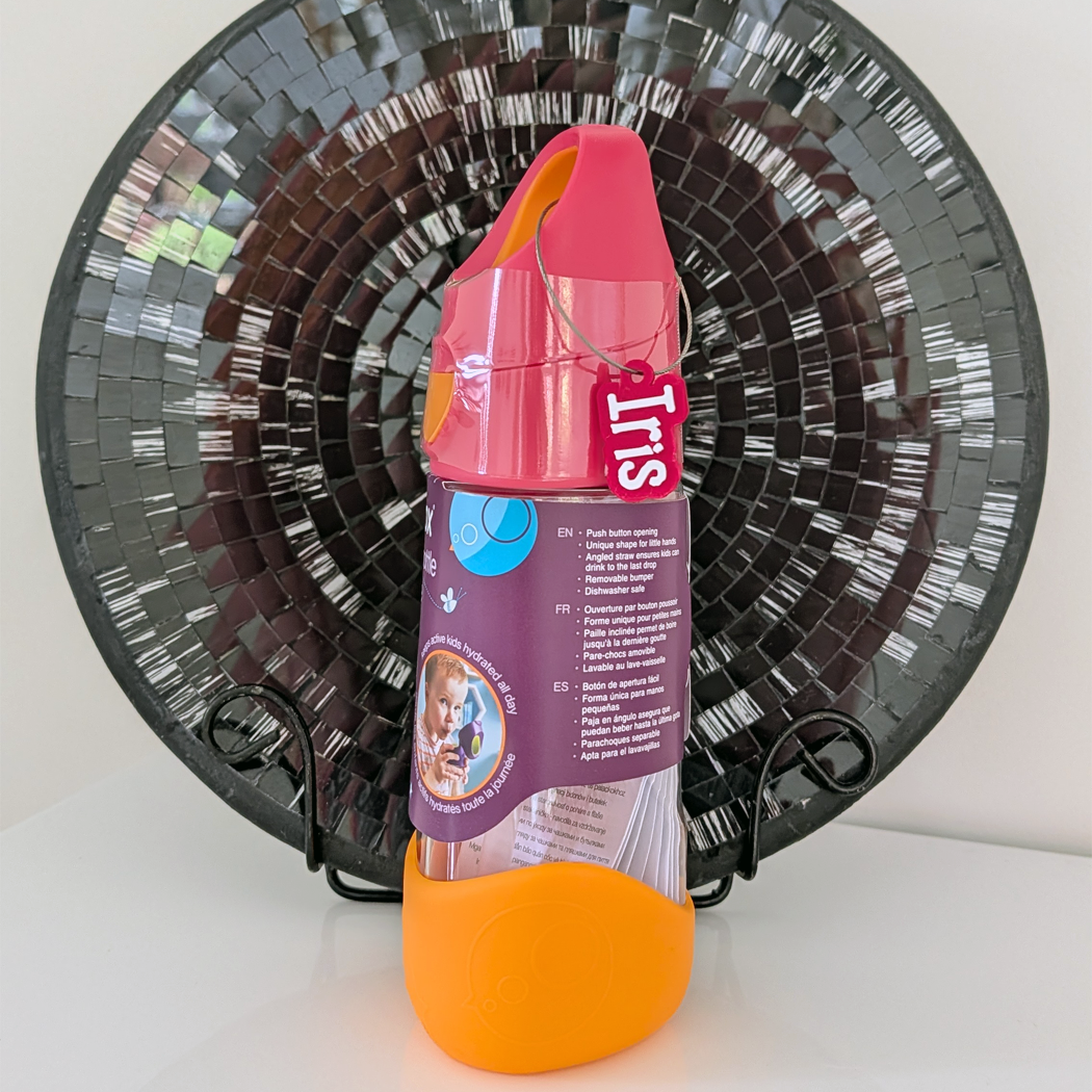 Colorful bottle with a label featuring a baby's face, against a decorative black and silver fan.