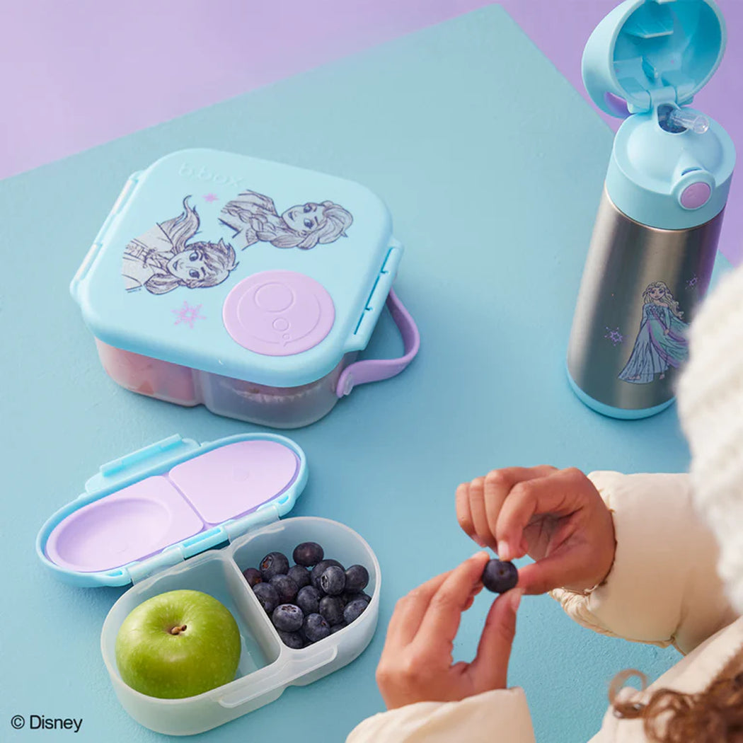 Frozen-themed lunch box, snack container, and water bottle on a blue surface with a child's hand reaching for berries.