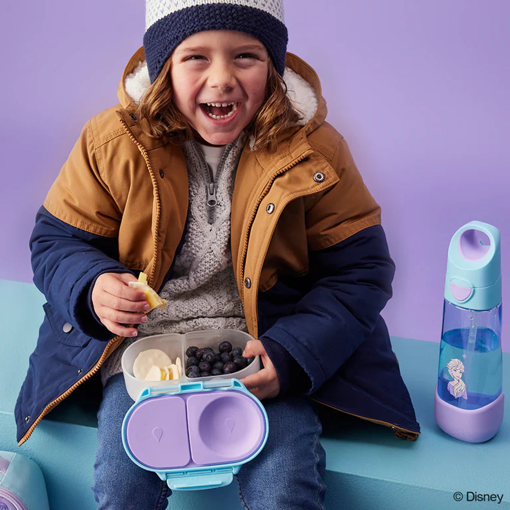 Child in winter clothing with a lunchbox and water bottle on a purple background