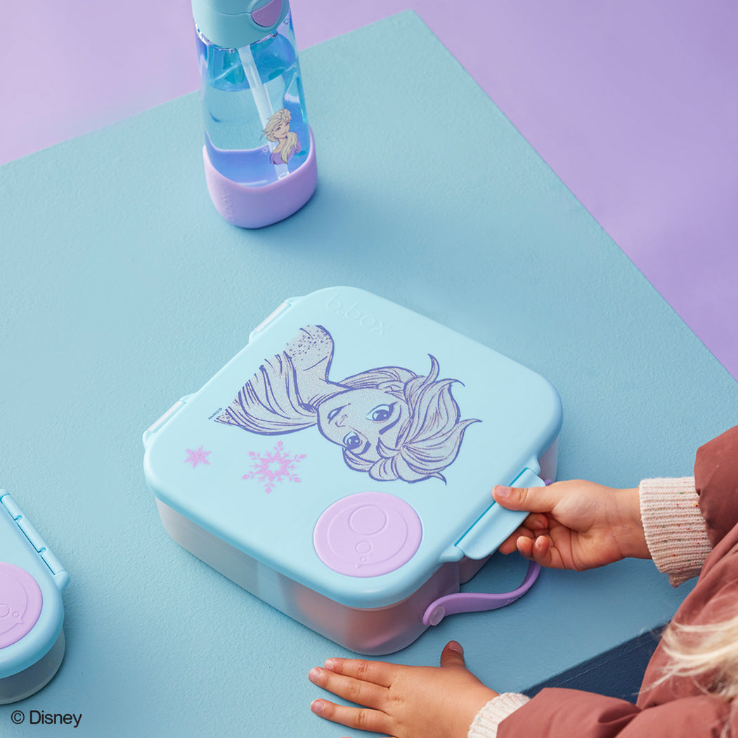 Children's lunch box with mermaid design on a blue surface, next to a water bottle.