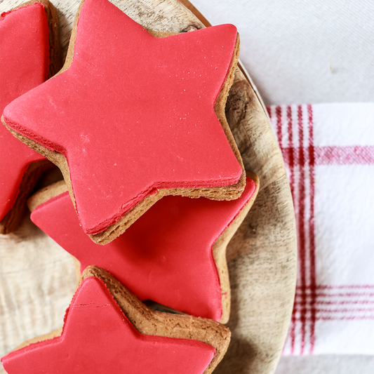 Red star-shaped cookies on a wooden plate with a red and white checkered towel in the background.