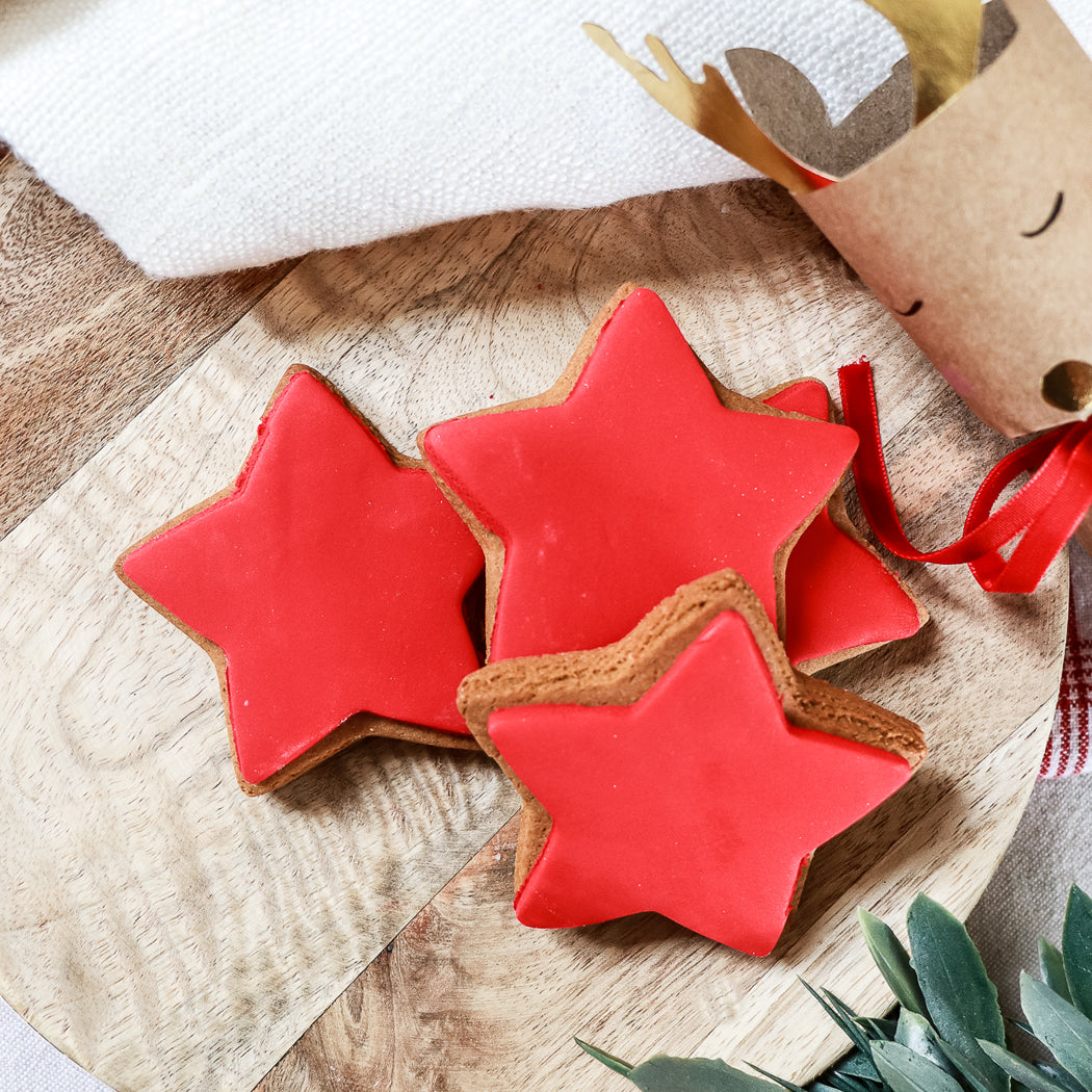 Red star-shaped cookies on a wooden surface with a decorative reindeer in the background.