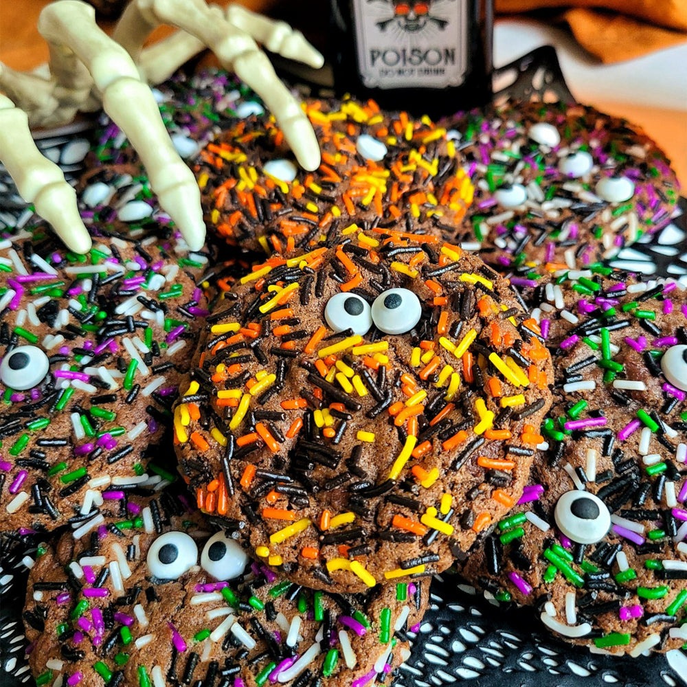 Halloween-themed cookies with sprinkles and candy eyes on a black plate.