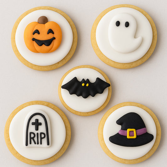 Halloween-themed cookies with pumpkin, ghost, bat, tombstone, and witch hat designs on a light background.