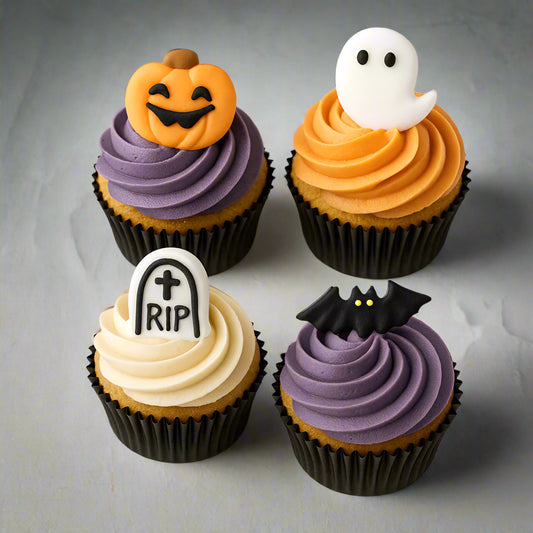 Four Halloween-themed cupcakes with decorative toppers on a white background