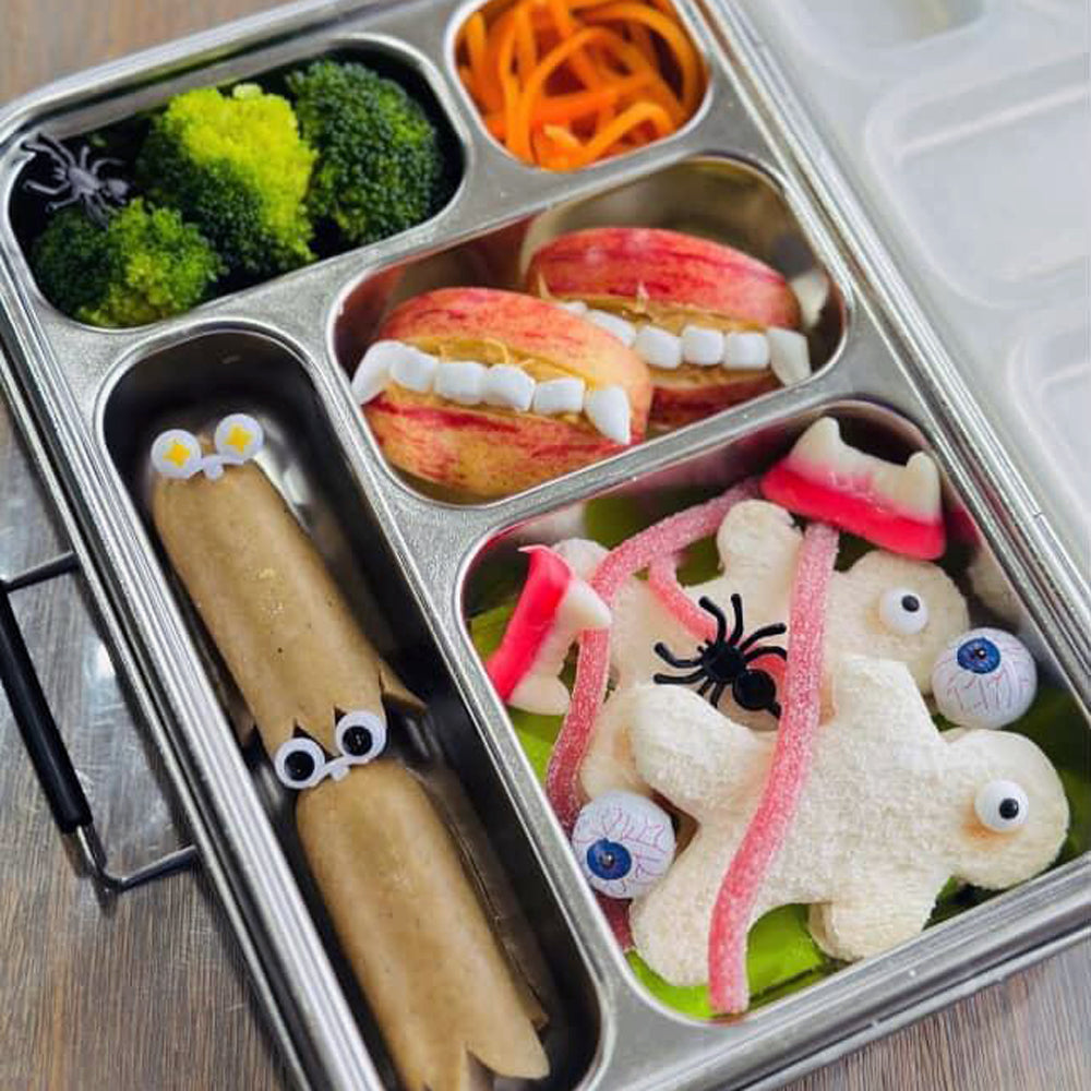 Halloween-themed bento box with food art including sausages, apples, and cookies.