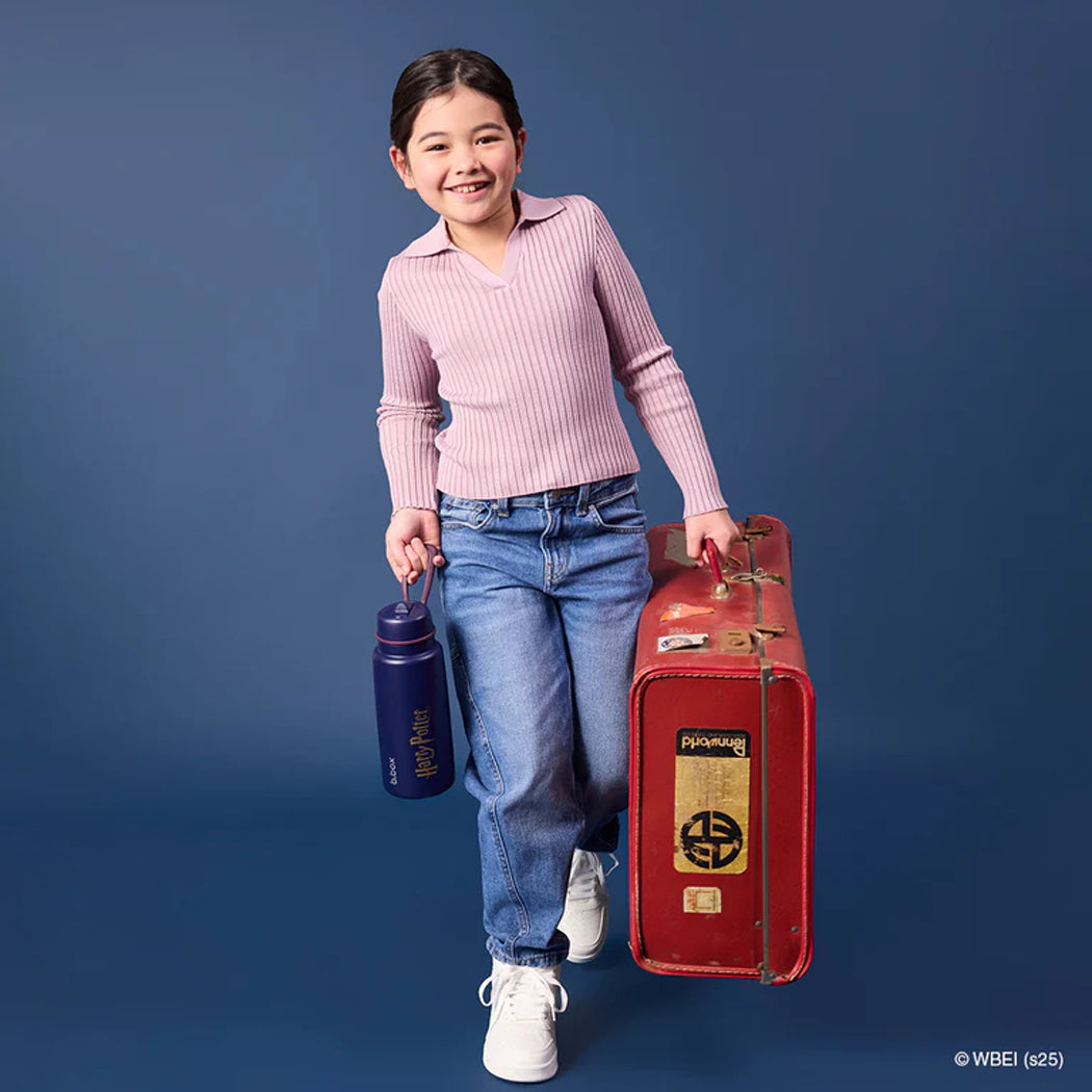 Young girl holding a red suitcase and blue water bottle against a dark blue background