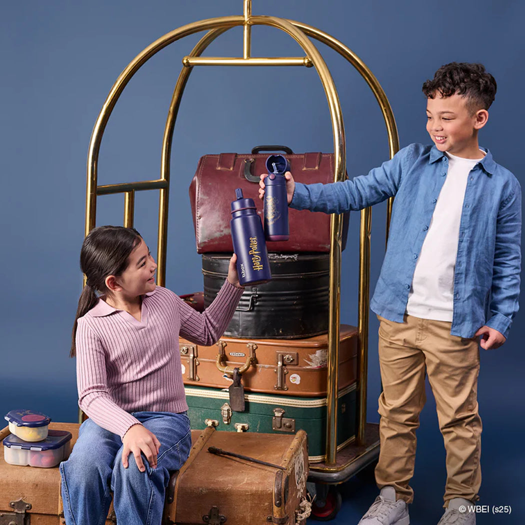 Two children with vintage suitcases and a luggage cart against a blue background