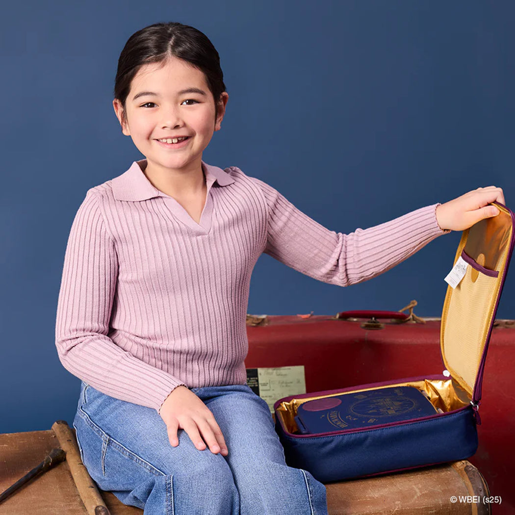 Young girl with a pink sweater and blue jeans sitting next to an open suitcase on a blue background