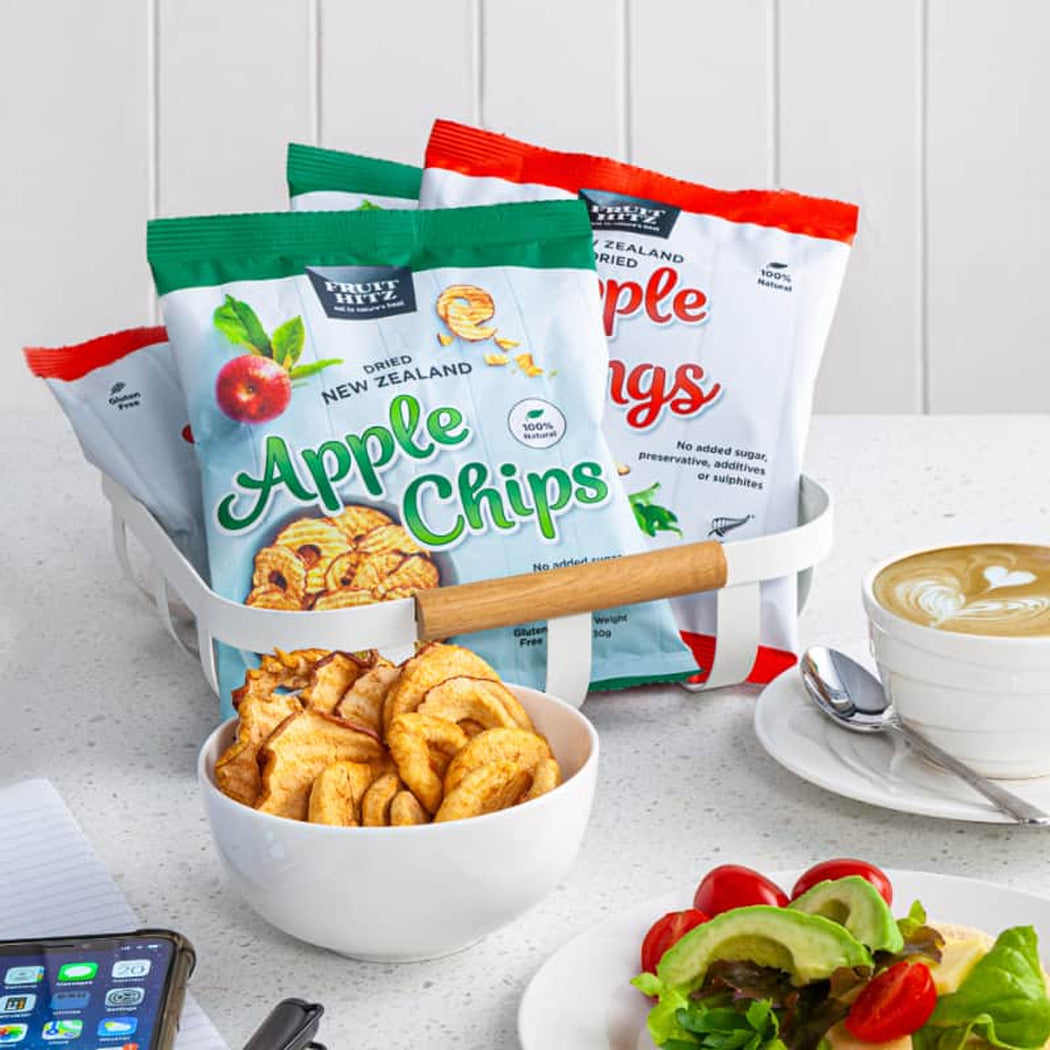Fruit Lizz apple chips in a bowl with packaging and a cup of coffee on a table.