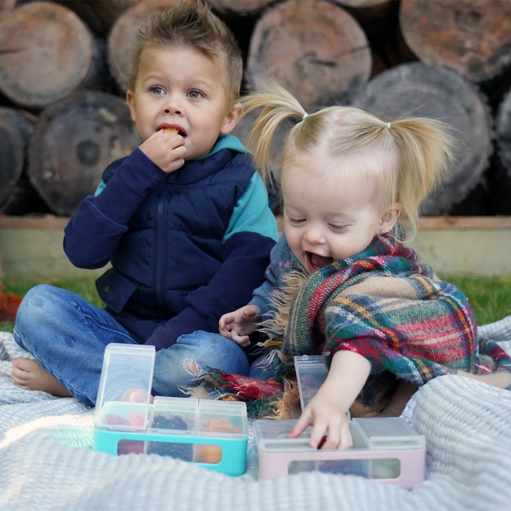 Two children playing with colorful toys outdoors on a blanket.
