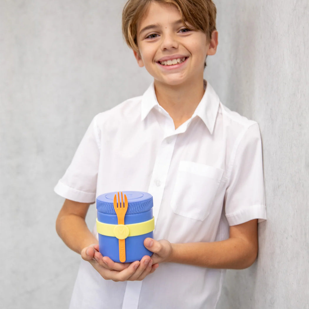 Child holding a blue container with a yellow lid and fork design against a plain background