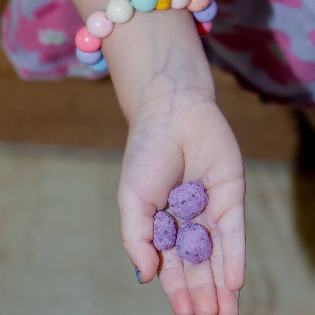 Child's hand holding purple balls with a colorful beaded bracelet on a blurred background