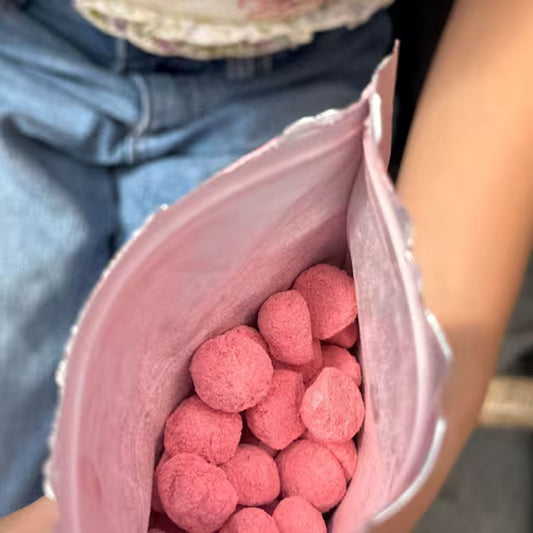 Pink candy balls in an open pink bag held by a person.