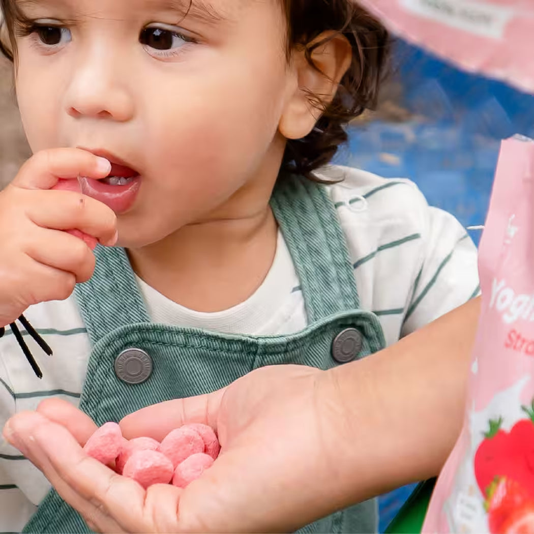 Child holding pink candies with a strawberry yogurt container in the background