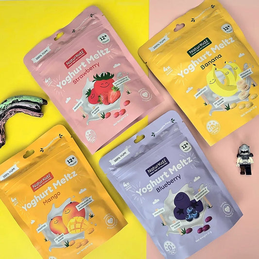 Four colorful packages of Yoghurt Meltz with strawberry, banana, mango, and blueberry flavors on a yellow and pink background.