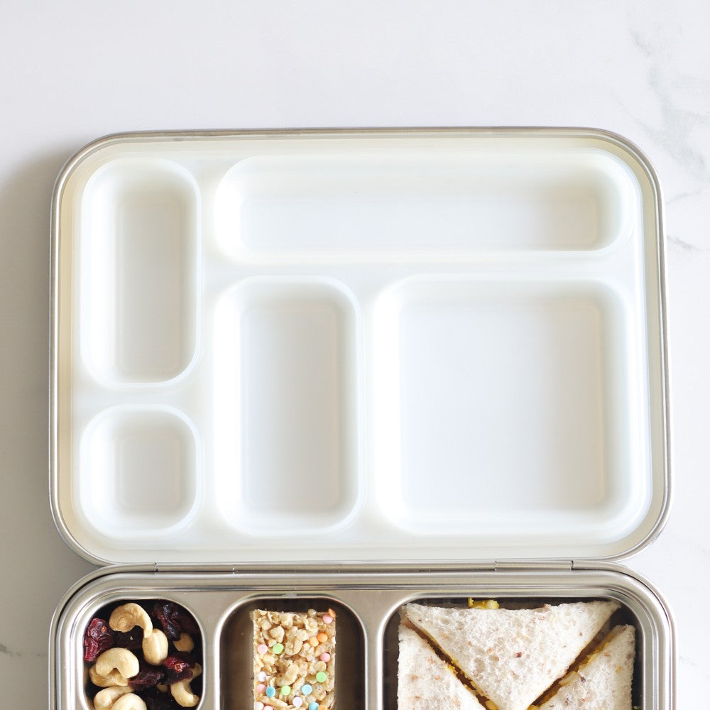 Meal prep container with compartments containing a sandwich, nuts, and other snacks on a white background