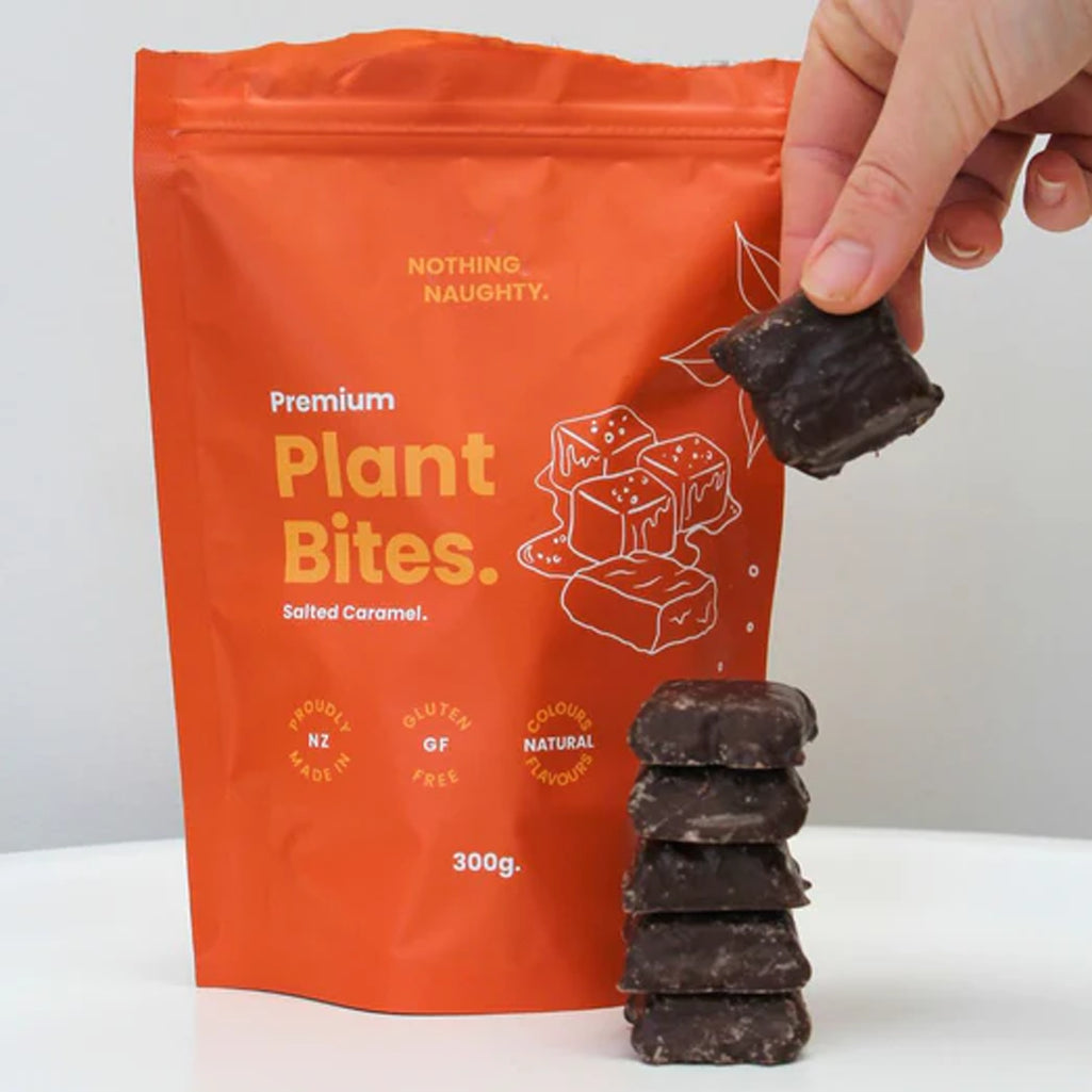 Hand holding a packet of 'Plant Bites' with a stack of chocolate bars on a white background