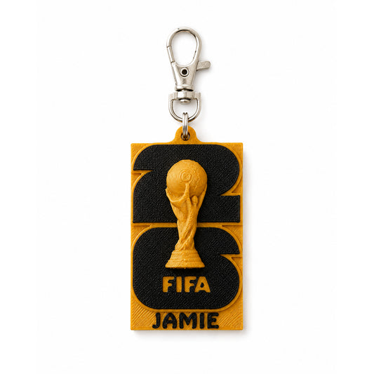 A rectangular keychain featuring with a custom name, 'JAMIE'. The keychain has a textured black and gold background.
