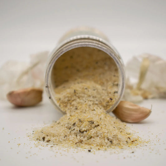 Open jar of dried herbs with garlic cloves on a light background