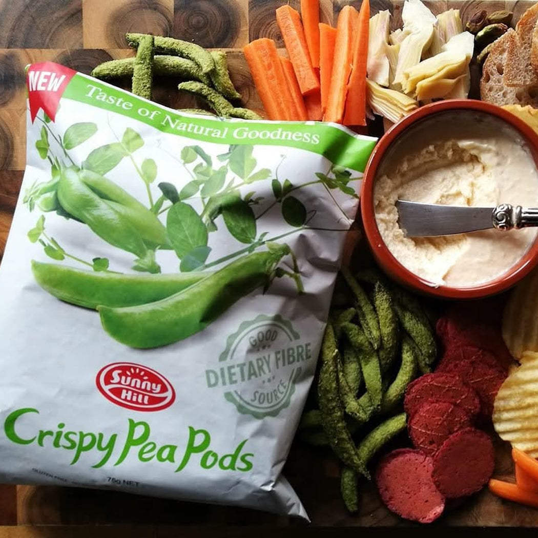 Bag of Sunny Hill Crispy Pea Pods with a snack platter including chips, carrots, and dip.