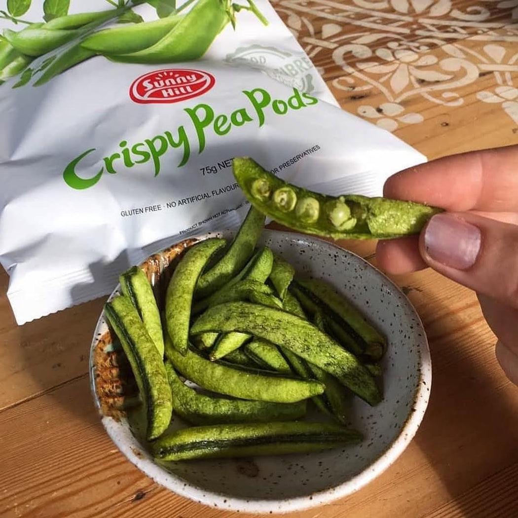 Crispy pea pods being held above a bowl with a Sunny Hill branded bag in the background.
