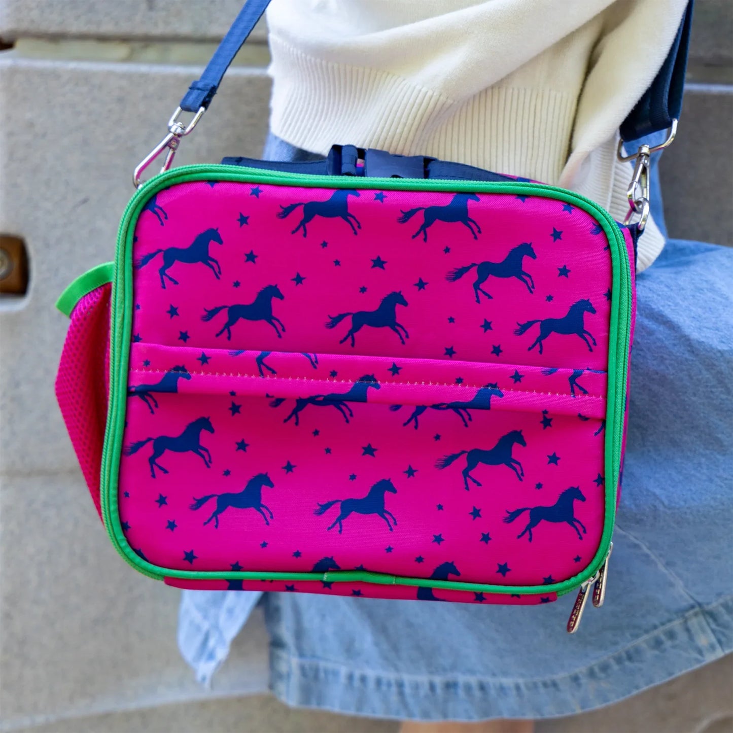 Pink lunch bag with horse pattern held by a person wearing a white sweater and blue jeans.