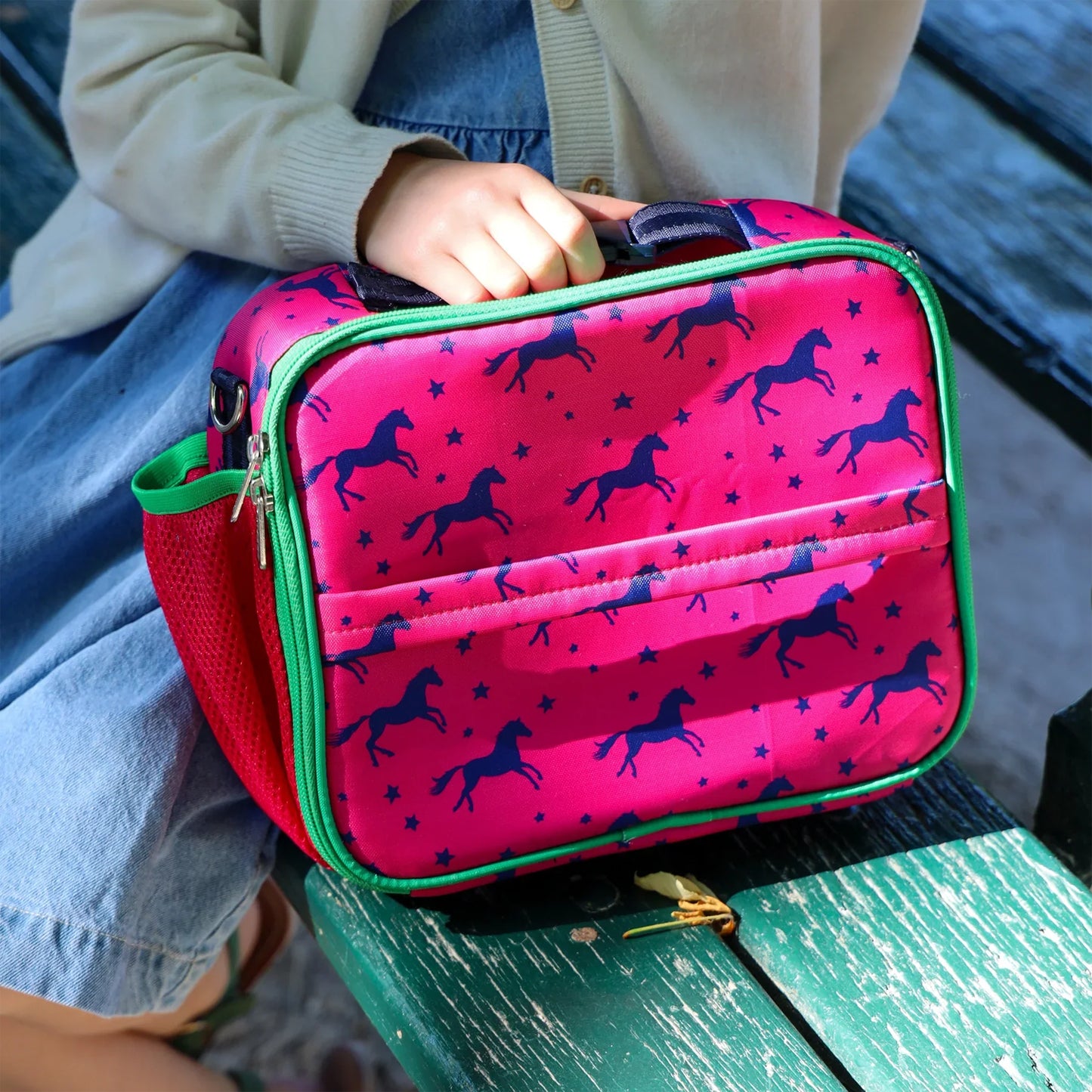 Pink lunch bag with horse pattern held by a person on a green bench
