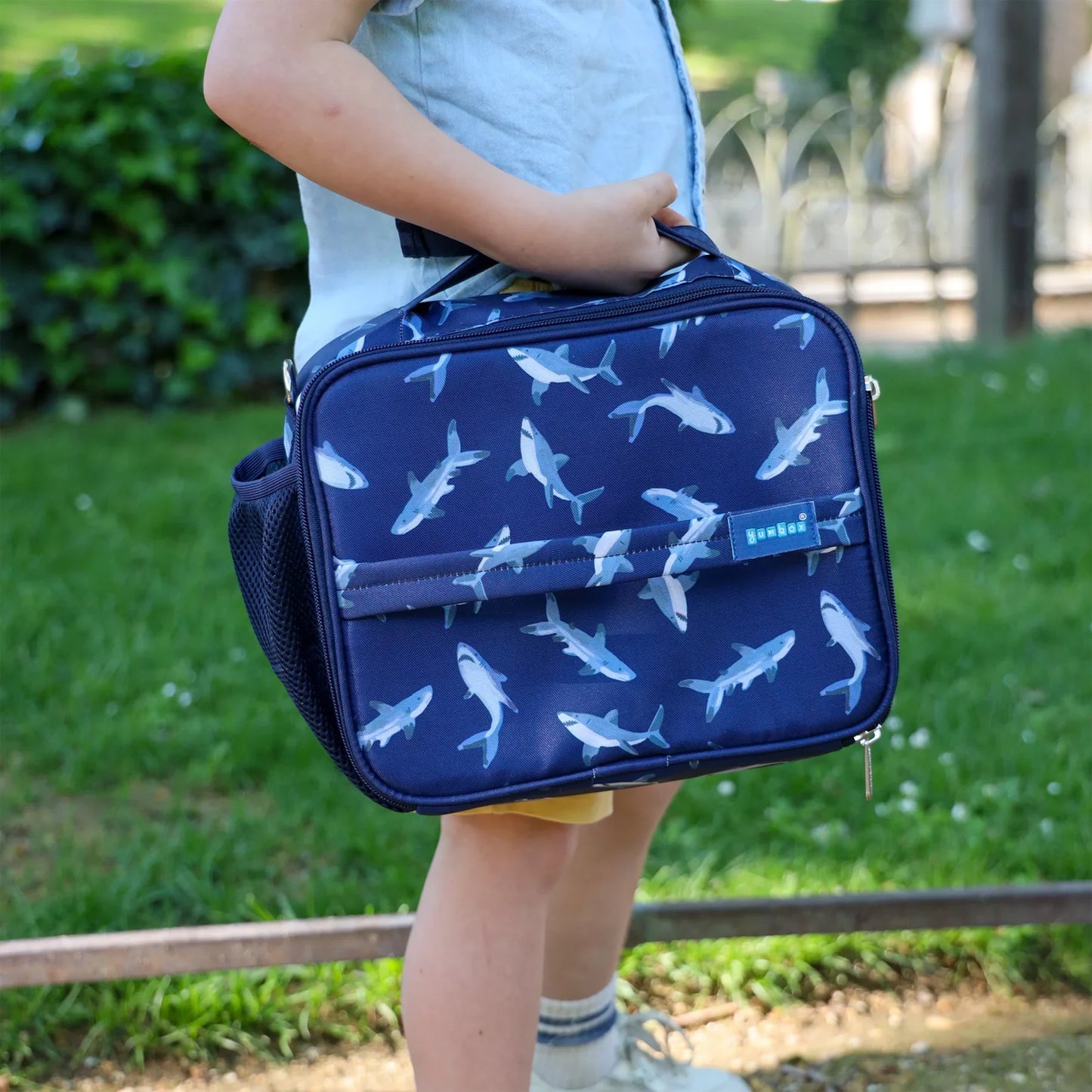 Child holding a navy blue bag with shark pattern outdoors
