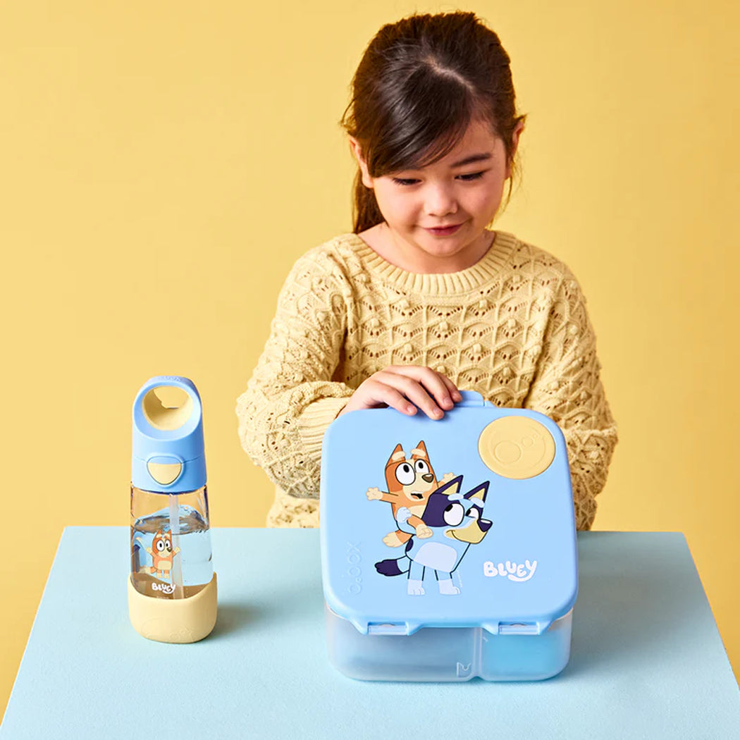 Child holding a blue lunch box with cartoon character design on a yellow background