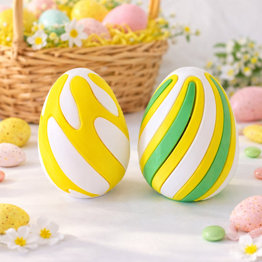 Two decorative Easter eggs with yellow, white, and green stripes on a table with a basket of Easter eggs in the background.