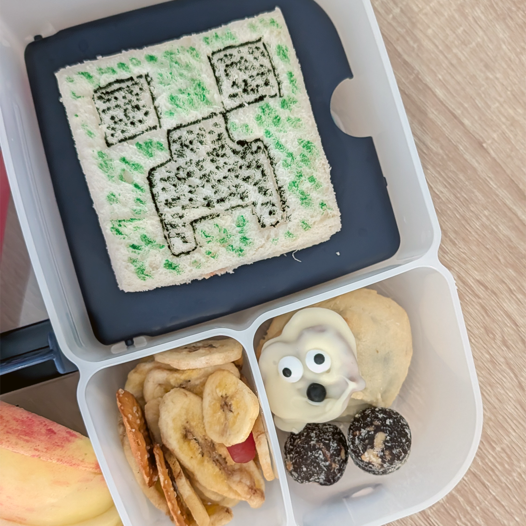 Bento box with a square sandwich, dried fruit, and a cookie shaped like a dog.