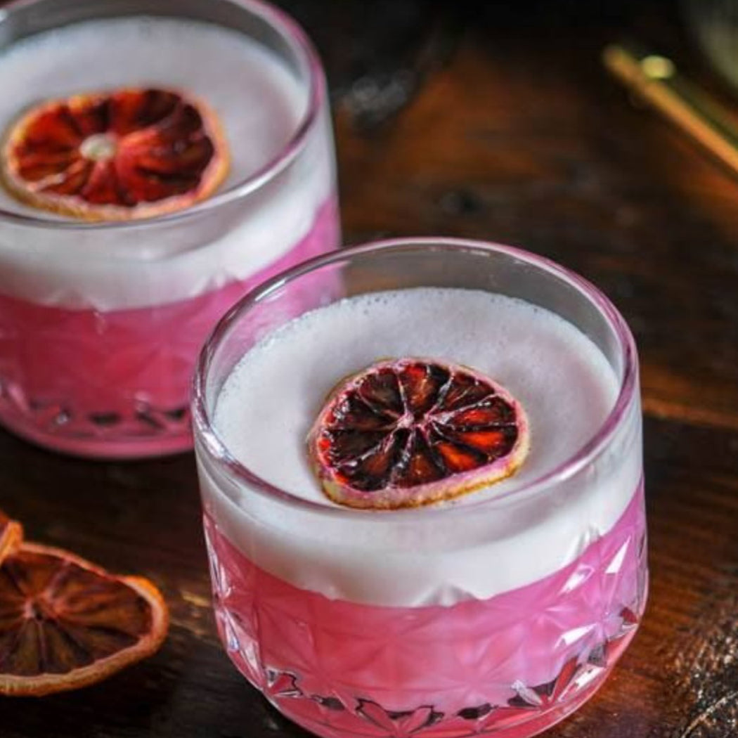 Two glasses of pink cocktail with blood orange slices on a wooden surface