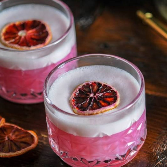 Two glasses of pink cocktail with blood orange slices on a wooden surface