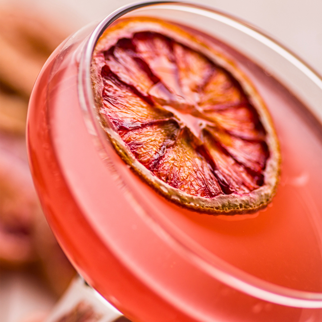 One glass of a pink cocktail with blood orange slices inside