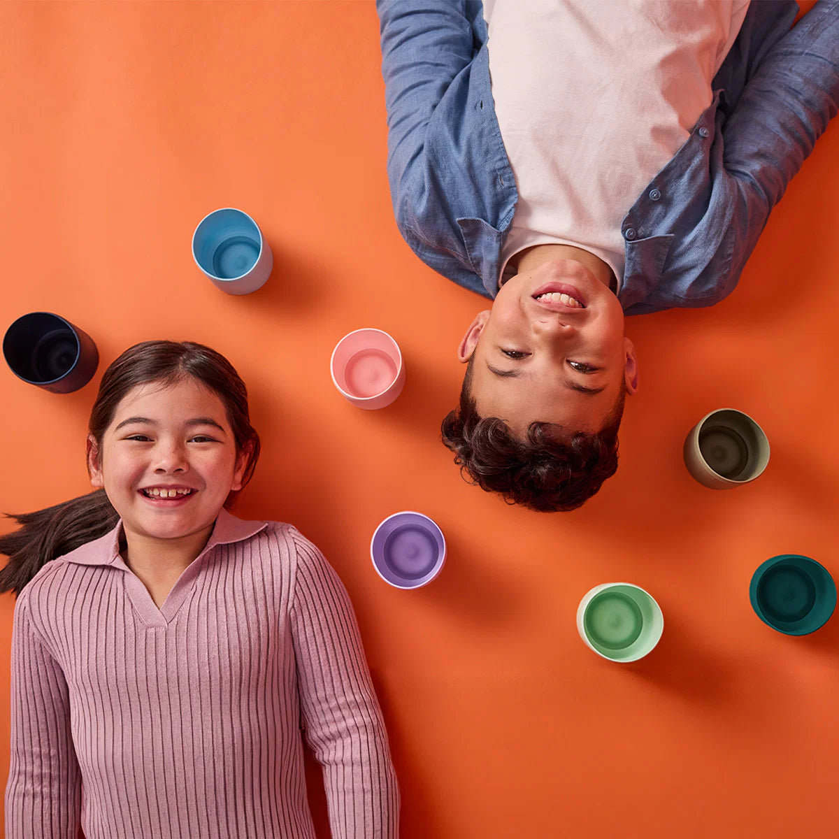 Two children standing on an orange surface with colorful cups around them.