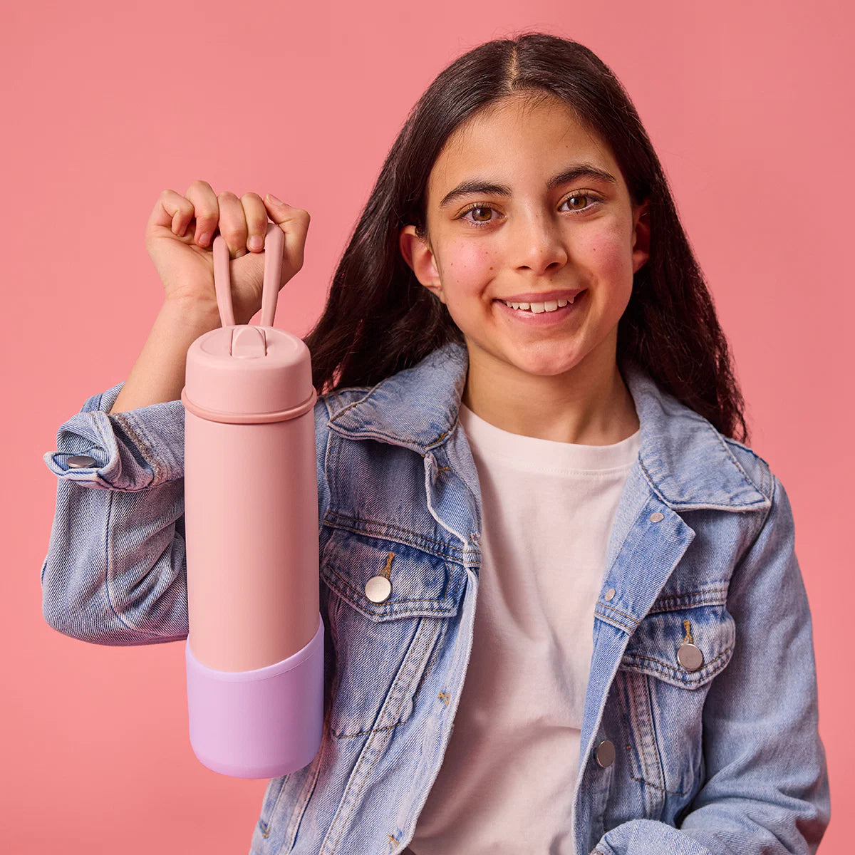 Young girl holding a pink and purple cylindrical container against a pink background