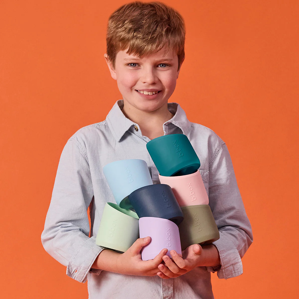 Child holding colorful cups against an orange background