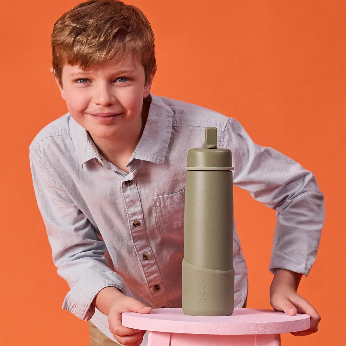 Child holding a green water bottle on a pink tray against an orange background